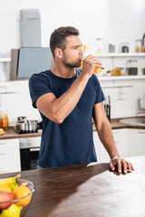 Fototapeta na wymiar man drinking orange juice near fresh fruits on blurred foreground on table
