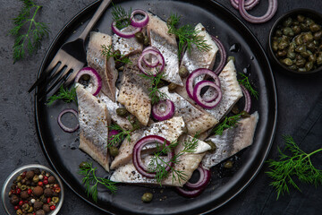 pickled herring with  red onion, capers and dill on black plate