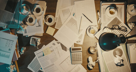 Messy office desk with paperwork and coffee cups