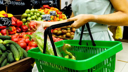 Unrecognizable caucasian woman with shopping basket is choosing vegetables in grocery store.
