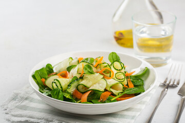 Green vegan salad from spinach leaves, cucumbers and carrots. Onon white concrete table. Copy space.