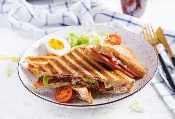 Grilled club sandwich panini with ham, tomato, cheese, avocado and cup of coffee. Delicious breakfast or snack.