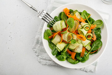 Green vegan salad from spinach leaves, cucumbers and carrots. Top view on white concrete table.