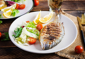 Delicious grilled dorado or sea bream fish with salad, spices, grilled dorada on a wooden table.