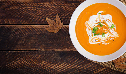 Pumpkin soup on rustic wooden table. Seasonal autumn food - Spicy pumpkin and carrot soup. Top view, flat lay, copy space