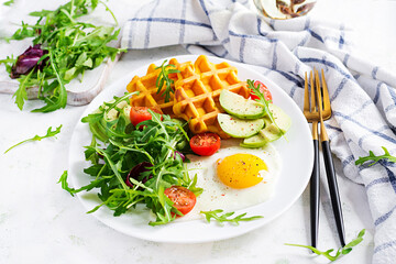 Breakfast with pumpkin waffles, fried egg, tomato, avocado and arugula on white background. Appetizers, snack, brunch. Healthy vegetarian food.