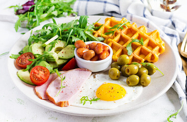 Breakfast with pumpkin waffles, fried egg, ham, tomato, avocado, beans and olives on white background. Appetizers, snack, brunch. Healthy food.