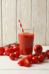 Glass with tomato juice and straw and tomatoes on wooden background