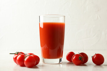 Glass of tomato juice and tomatoes on white textured background
