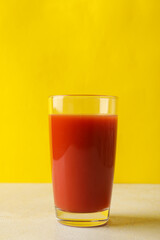 Glass of tomato juice against yellow background