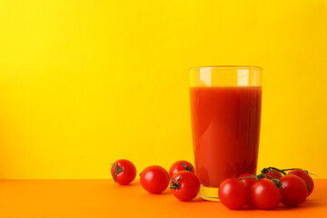 Glass of tomato juice and tomatoes against yellow background