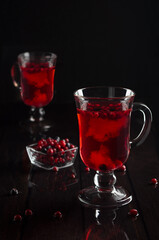 Red fruit tea with cowberry, blueberry in two transparent glasses on  black wood table in dark interior, vertical.