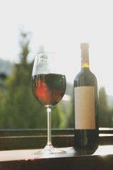 Glass and bottle of red wine on wooden windowsill against mountain background