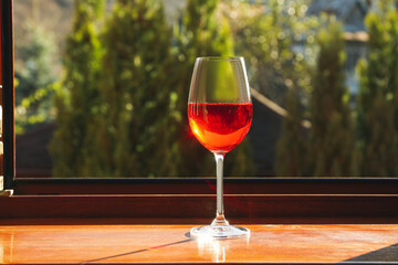 Glass of red wine on wooden windowsill in sunny weather