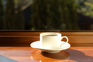 Saucer with cup of hot drink on wooden windowsill