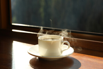 Saucer with cup of hot drink on wooden windowsill