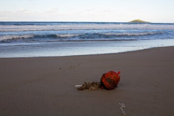 evocative closeup image of abandoned buoy on sandy beach with rough seas and
small island in the background