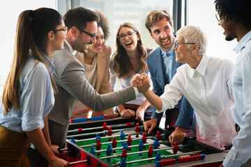 Business people having great time together. Colleagues playing table football in office. - obrazy, fototapety, plakaty