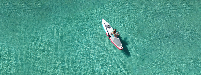 Aerial drone ultra wide top down photo of fit unidentified woman paddling on a SUP board or Stand Up Paddle board in Caribbean tropical turquoise exotic bay - obrazy, fototapety, plakaty