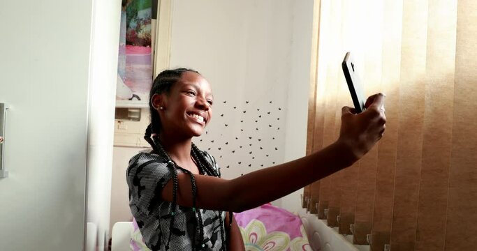 Teenager girl taking selfie in adolescent room. Mixed race black ethnicity