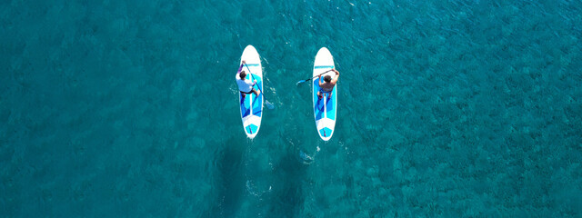 Aerial drone ultra wide photo of 2 men exercising sup board or Stand Up Paddle board in turquoise...