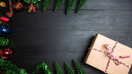 A gift box made of brown paper, tied with a red white bowstring, placed on a wooden board decorated with Christmas trees and colorful bells copy space for text. giving for Holiday, celebration object