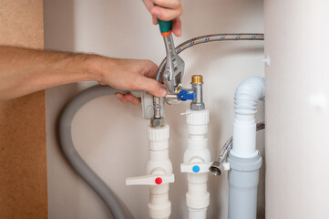 A man uses an adjustable wrench to install a water supply hose in the dishwasher.
