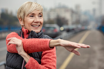 Active senior woman stretches her muscles before running through the city during the day.