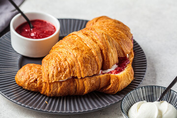 Fresh croissant with cream and berry jam on gray plate. Delicious breakfast concept.