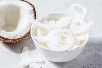 Raw coconut chips in white bowl, gray background. Vegan food concept.