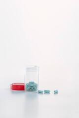 open transparent pill bottle with some pills outside and red caps on the white ground