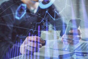 Double exposure of man's hands holding and using a phone and financial graph drawing. Analysis concept.