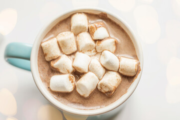A mug of chocolate drink with marshmallows on a light background with bokeh.