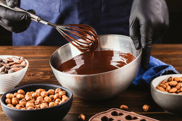 Confectioner prepares the melted dark chocolate in a bowl on a wooden table. Liquid hot chocolate....