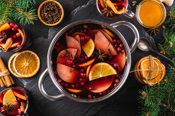 Top-down view of cooking pot of hot wine with aromatic spices on a black textured background. Christmas mulled wine. New Year's warming drink.