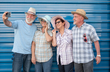 A smiling group of four people in friendship wearing straw hats, looking at smartphone for a selfie together. Carefree senior women and men enjoying retirement