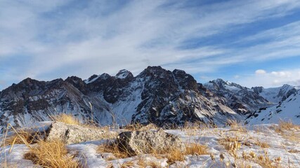 Clouds move over the tops of snow-capped rocks. Evening mountain landscape in winter. Panoramic view of mountains with rocks and ice in the Tien Shan mountains in Central Asia near Almaty. Timelapse