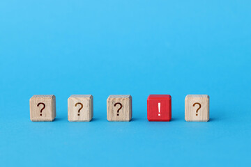 Red wooden cube with exclamation mark lying among cubes with question marks closeup
