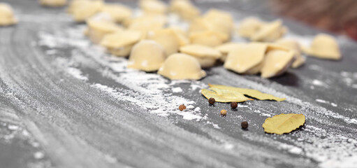 The background is a black table, sprinkled with flour, smeared by hand, on it are dumplings, in the...