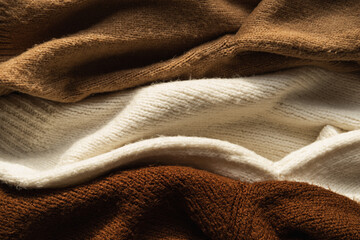 Three colorful warm woolen winter sweaters / pullovers. Beige, white, brown. Minimal fashion composition. Flat lay, top view.