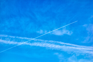 Airplane and its contrail in a blue sky with clouds.