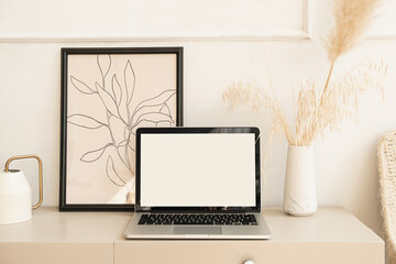 Laptop computer with blank screen pastel beige on table with boho decorations. Pampas grass...