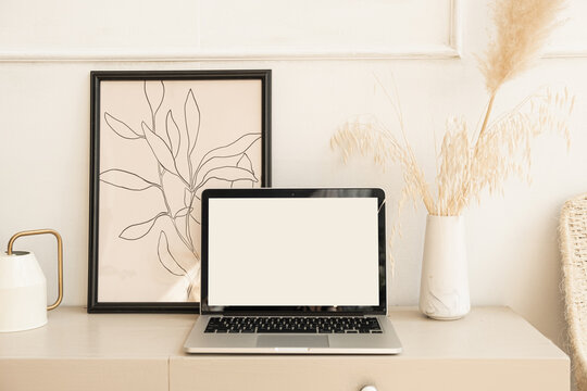 Laptop computer with blank screen pastel beige on table with boho decorations. Pampas grass bouquet, photo frame. Minimal boho styled interior design template with mockup copy space.