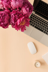 Home office desk workspace with laptop, pink peony flowers bouquet on peach background. Flat lay, top view blog, website, social media concept.