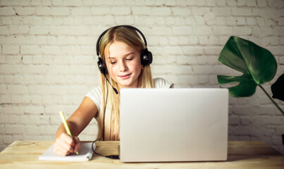 Children home schooling, teenage girl in headphones studying online at home, e-learning concept