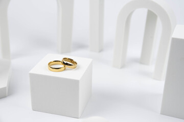 Golden wedding rings on trendy white podium. Aesthetic still life art photography.