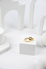 Golden wedding rings on trendy white podium. Aesthetic still life art photography.