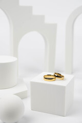 Golden wedding rings on trendy white podium. Aesthetic still life art photography.