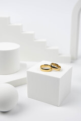 Golden wedding rings on trendy white podium. Aesthetic still life art photography.