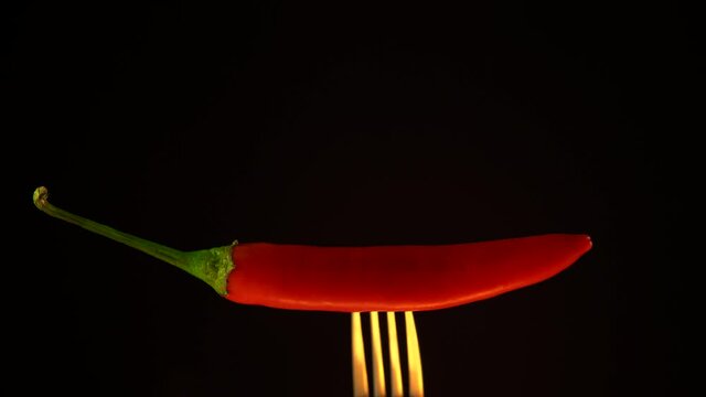 Red hot chili pepper on frok in fire, black background